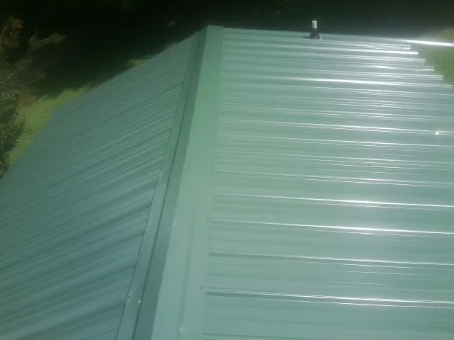 New green metal panels meeting at the ridge of a roof — Flat Roof Repair work by our crew in Wolcott