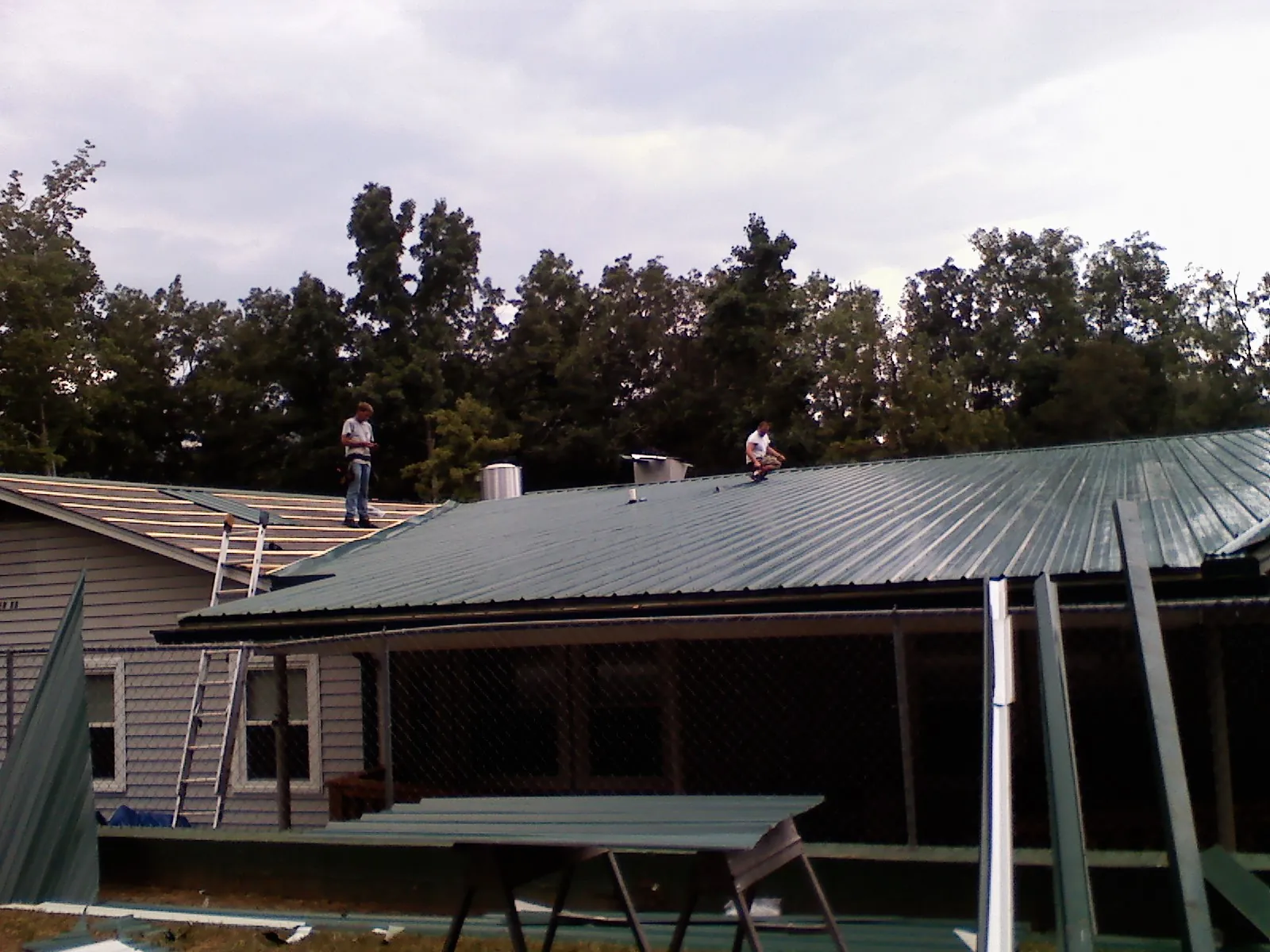 Two roofers installing green metal panels above a covered porch in Wolcott